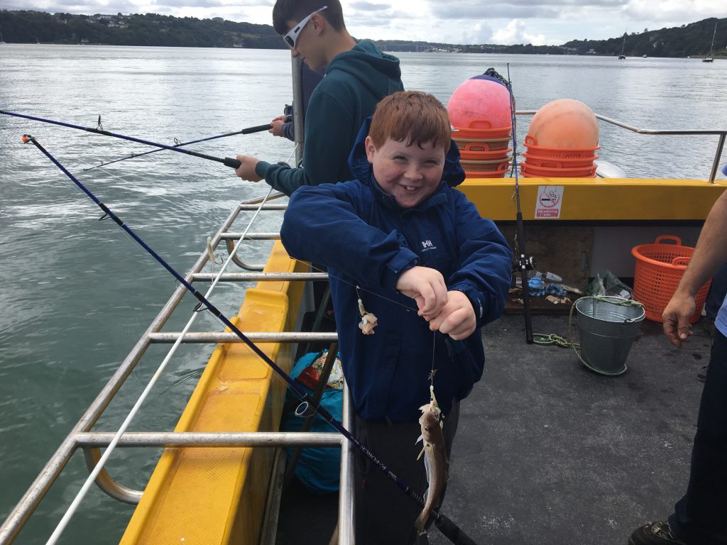 The picture shows a young boy while out on a Starida fishing trip, he has caught a small fish and is smiling