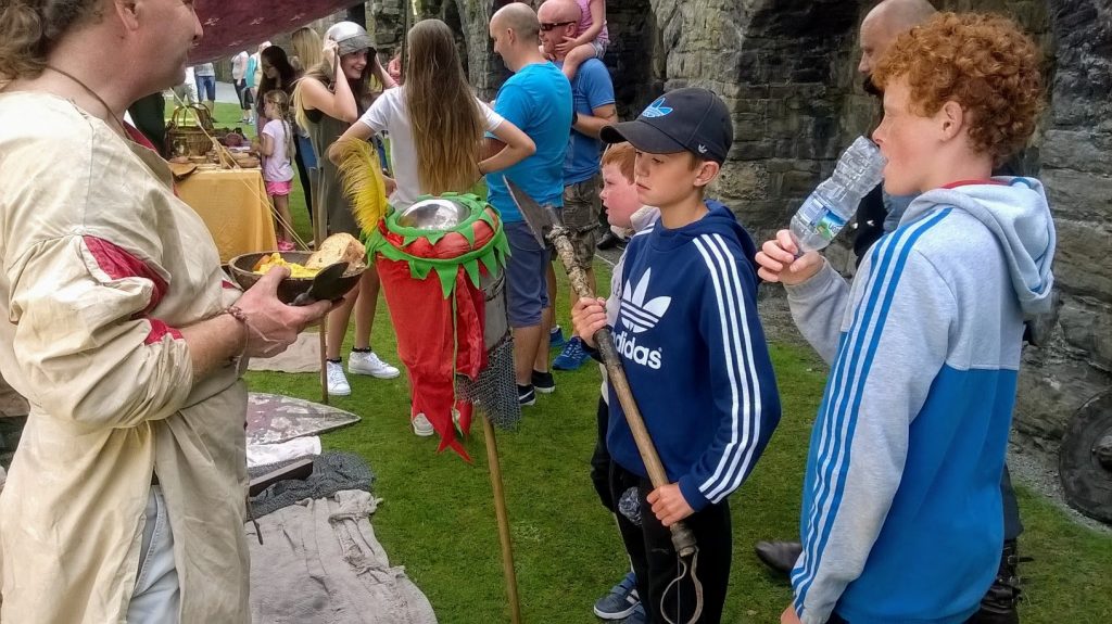 children gathered around a medieval enactment tent, they are being shown weapons of the era, at Beaumaris Castle
